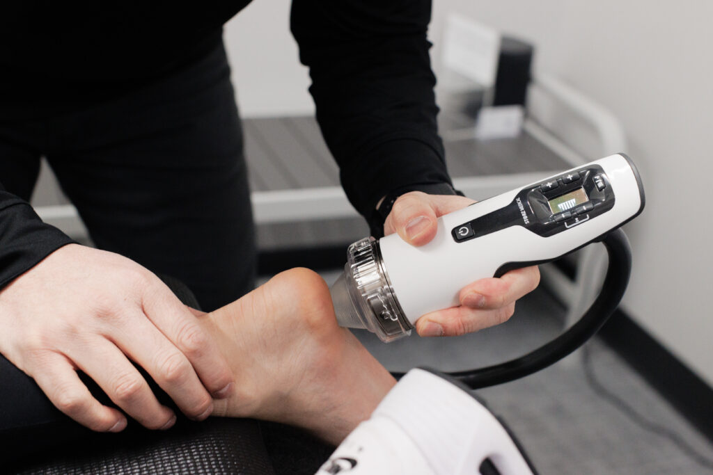 Patient receiving focused shockwave therapy on the heel using a medical-grade device for plantar fasciitis treatment.